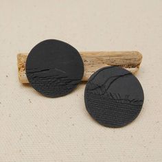 two black round buttons sitting on top of a piece of wood next to a stick