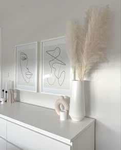 two pictures on the wall above a dresser with vases and feathers in front of it