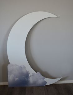 a white paper cut out of the shape of a crescent with clouds in the background