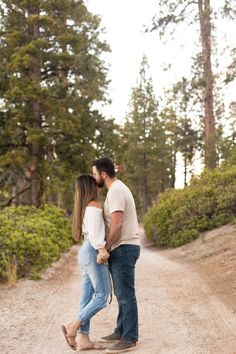 a man and woman kissing on the side of a dirt road in front of trees