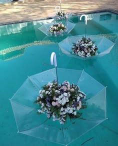 two umbrellas with flowers in them sitting on the ground next to a swimming pool