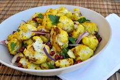 a white bowl filled with cauliflower, onions and garnishes on top of a table