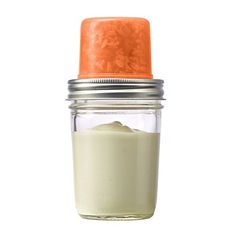 a glass jar filled with cream on top of a white table next to an orange lid