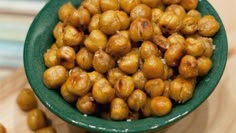 a green bowl filled with chickpeas on top of a wooden table