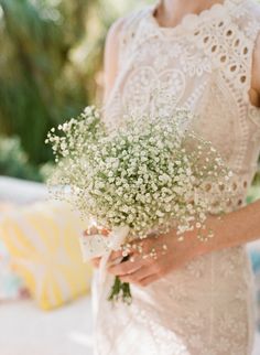 a woman holding a bouquet of baby's breath flowers in her hand and wearing a white dress