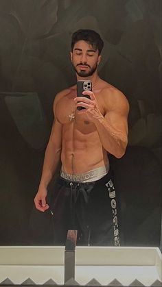 a shirtless man taking a selfie in front of a mirror with his cell phone