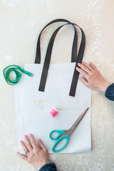 a woman's hands with pink nail polish and scissors on top of a white tote bag