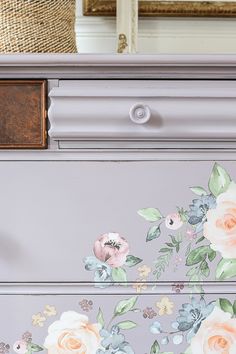 an old dresser painted with flowers and leaves on the top, next to a wicker basket