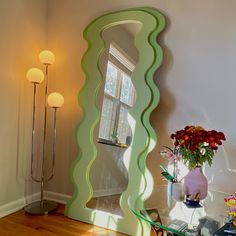 a large mirror sitting on top of a wooden floor next to a vase filled with flowers