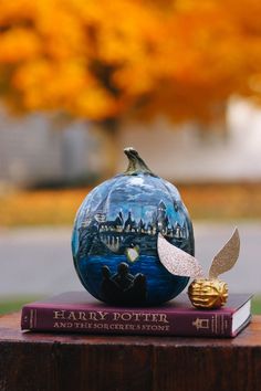 a harry potter pumpkin sitting on top of a book next to an orange tree with yellow leaves