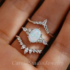 a woman's hand holding three rings with white opal and diamonds on them