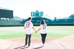 a man and woman holding hands on top of a baseball field with the city in the background