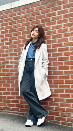 a woman leaning against a brick wall with her hands in her pockets and looking up