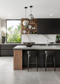 a modern kitchen with marble counter tops and black cabinets, along with two bar stools