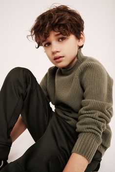 a young boy is sitting on the floor wearing a turtle neck sweater and black pants