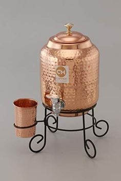 a large copper pot and two small cups on a stand with a metal cup holder