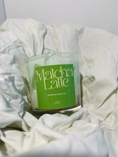 a candle sitting on top of a bed covered in white sheets and paper with the words matcha latte printed on it