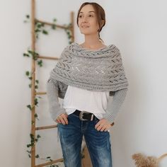 a woman standing in front of a ladder with her hands on her hips wearing a gray knitted shawl