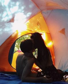 two people are sitting in front of a tent with the sun shining through it and one person is kissing the other