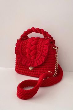 a red handbag with braided handles on a white surface, the bag has a gold chain around it