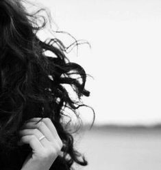 black and white photograph of a woman with curly hair looking at the camera while holding her hand near her face