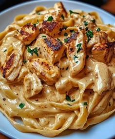 a pasta dish with chicken and sauce on a blue plate sitting on a wooden table