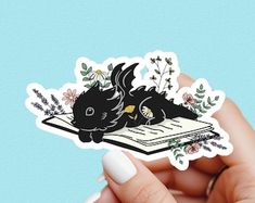 a hand holding a black cat sticker with flowers on it