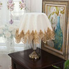 a lamp sitting on top of a wooden table next to a window with curtains behind it