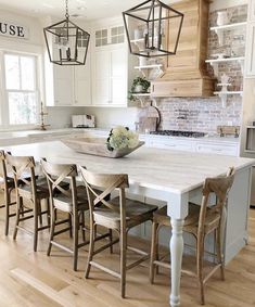 a kitchen with white cabinets and an island in the center, surrounded by wooden chairs