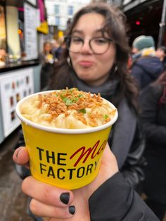 a woman holding up a yellow cup filled with food