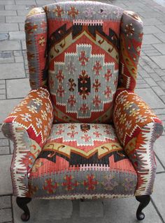 a colorful chair sitting on top of a brick floor next to a sidewalk with no one in it