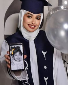 a woman wearing a graduation cap and gown holding a cell phone in front of balloons