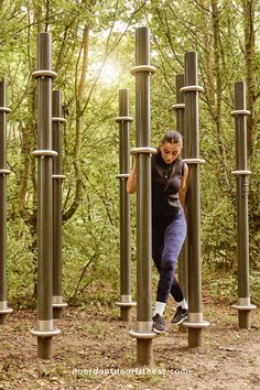 a woman climbing up and down metal poles in the middle of a forest with trees behind her