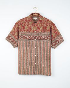 an orange shirt with paisley print on it hanging from a hanger in front of a white wall