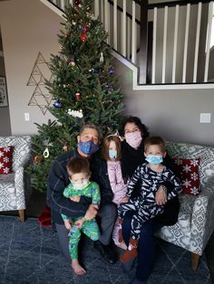 three adults and two children sitting in front of a christmas tree wearing facemasks