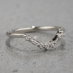 a white gold wedding ring with three stones on it's side, sitting on a gray surface