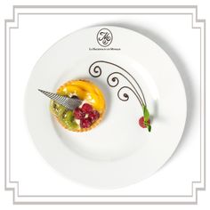 a white plate topped with a pastry covered in fruit next to a knife and fork