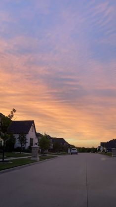 an empty street at dusk with houses in the distance and clouds in the sky above