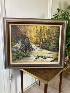 a painting is displayed on a table next to a potted plant