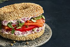 a bagel sandwich with salmon, lettuce and tomatoes on sesame seed bun