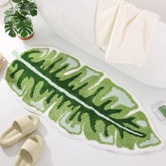 a bath mat with a large green leaf on it next to slippers and sandals