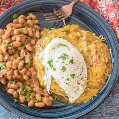 a blue plate topped with beans and an egg next to a fork on a table