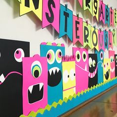 colorful paper monsters are lined up on the wall in front of a school hallway sign