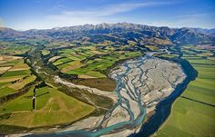 an aerial view of a river running through a green field with mountains in the background