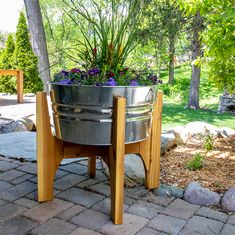 a metal bucket with flowers in it sitting on a wooden stand next to some rocks