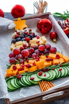 a platter filled with cheese, cucumbers and fruit on top of paper