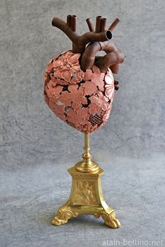 a heart shaped sculpture sitting on top of a gold pedestal with an iron pipe sticking out of it