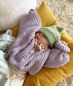 a baby wearing a sweater and pacifier laying on top of a yellow pillow next to pillows