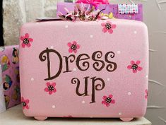 a pink suitcase that says dress up with flowers and polka dots on the front, sitting on a shelf