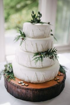 a three tiered white wedding cake with pine and evergreen decorations